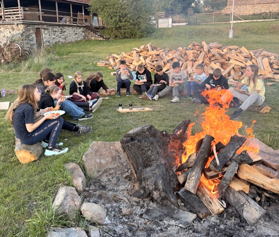 Děti sedí venku u ohně během tábora a BOT kempu.